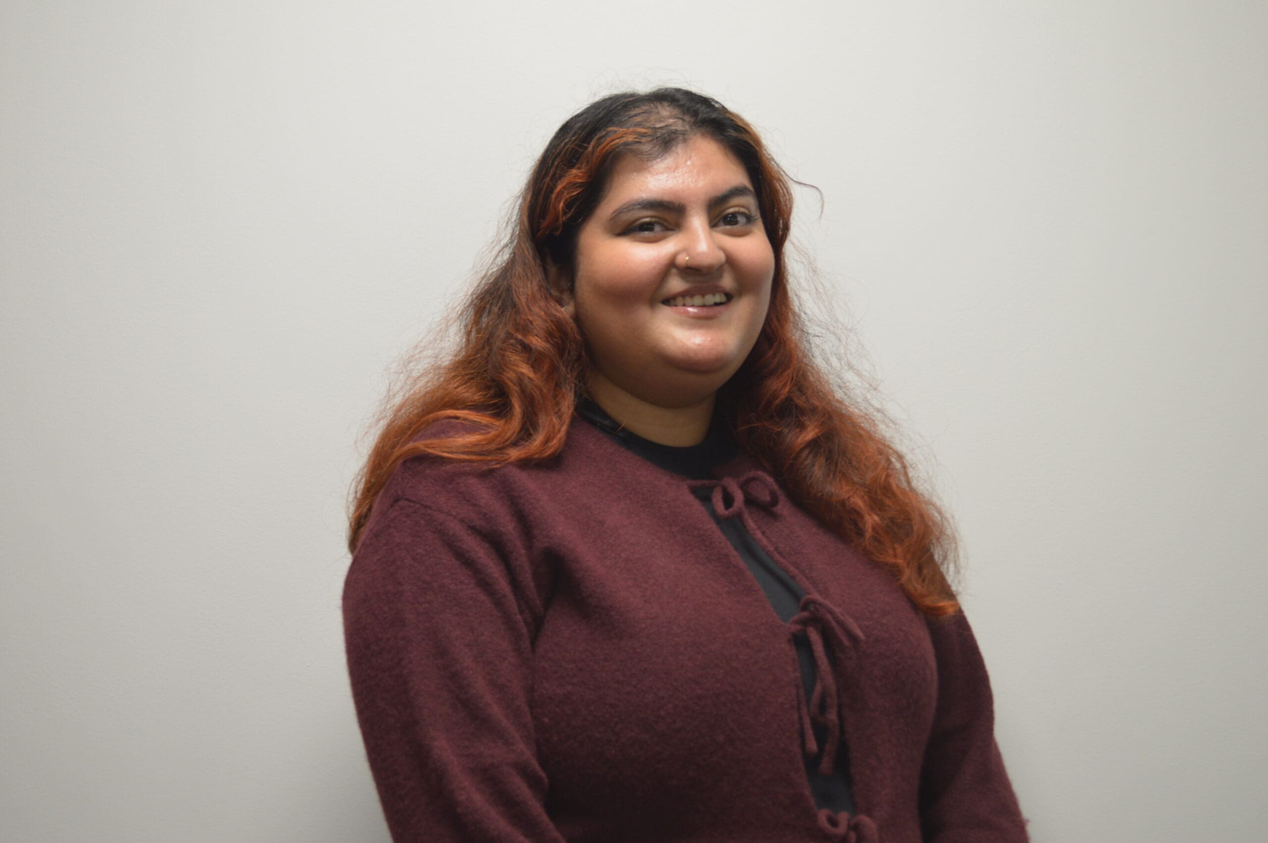 A photo of Maanya smiling in a red shirt with a gray backdrop