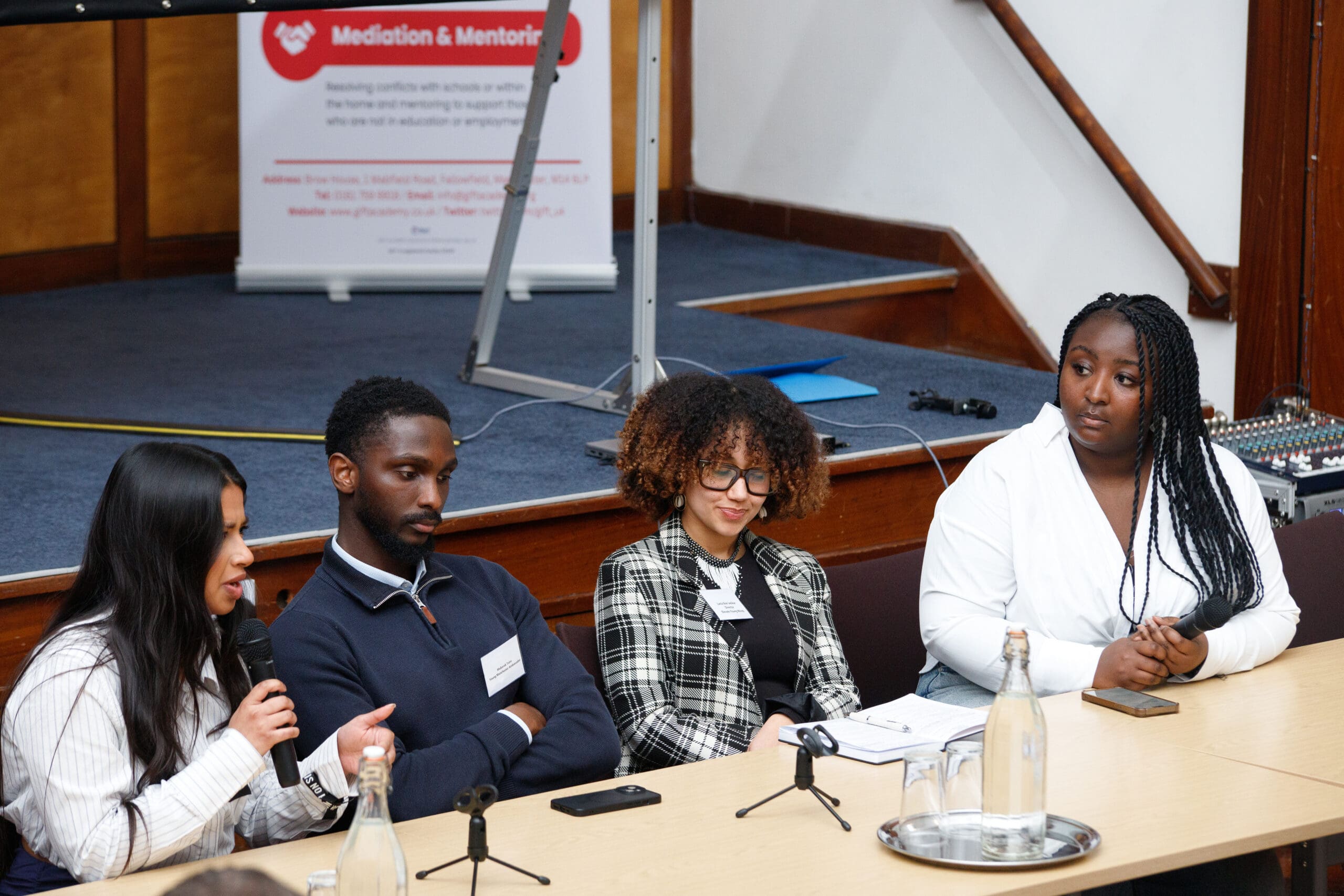 Three panelists and a presenter at the far right of the table during the Northern Cities Youth Employment Conference, engaged in discussion with microphones in front of them.