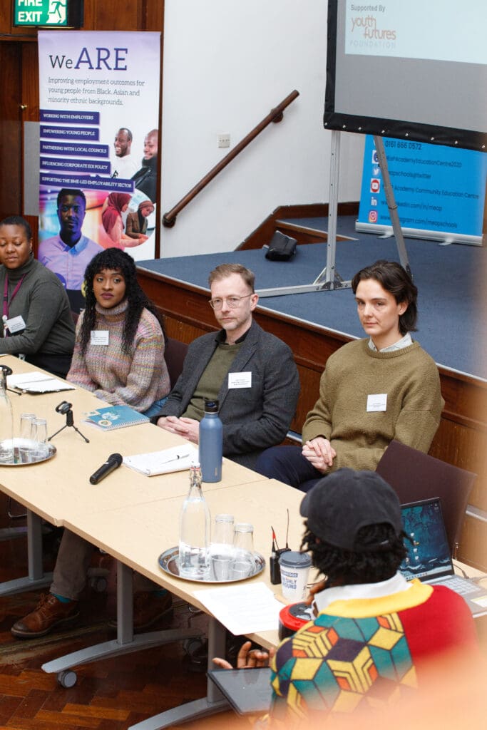 A group of panellists sat at a table during the Employer Panel at the Northern Cities Youth Employment Conference, listening to questions attentively with microphones in front of them.