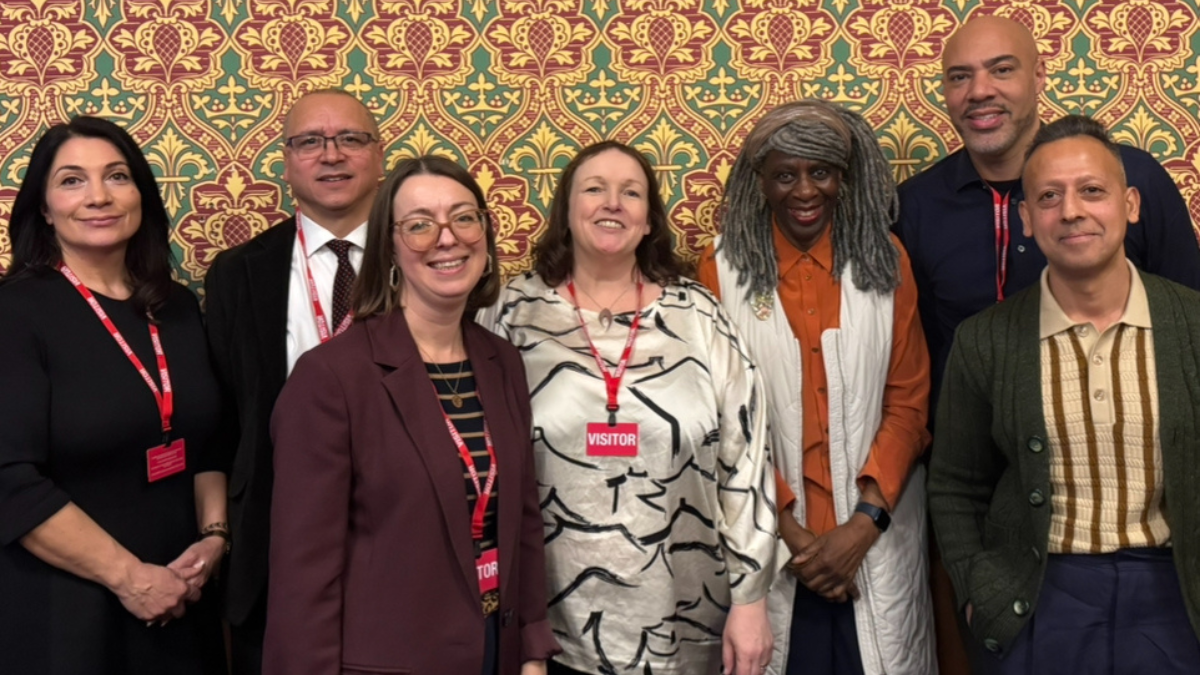 A group of seven diverse professionals stand together smiling. The group includes men and women of various ethnic backgrounds, dressed in smart-casual and professional attire.