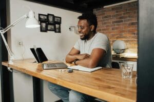 African American man smiling and working remotely from home using a laptop and digital tablet.
