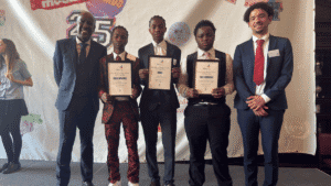 A group of five men, including three students holding award certificates, stand together for a photo in front of a colorful "Shine School Media Awards" backdrop.