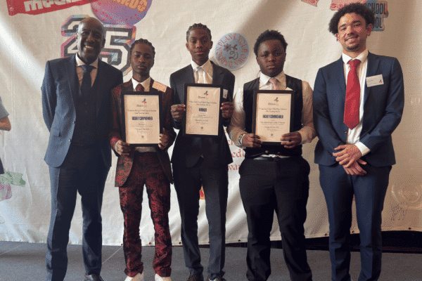 A group of five men, including three students holding award certificates, stand together for a photo in front of a colorful "Shine School Media Awards" backdrop.