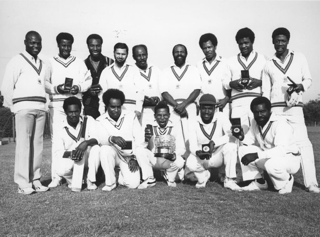 Group shot of LT Central Road Services cricket team in 1984 holding their medals and with a trophy.